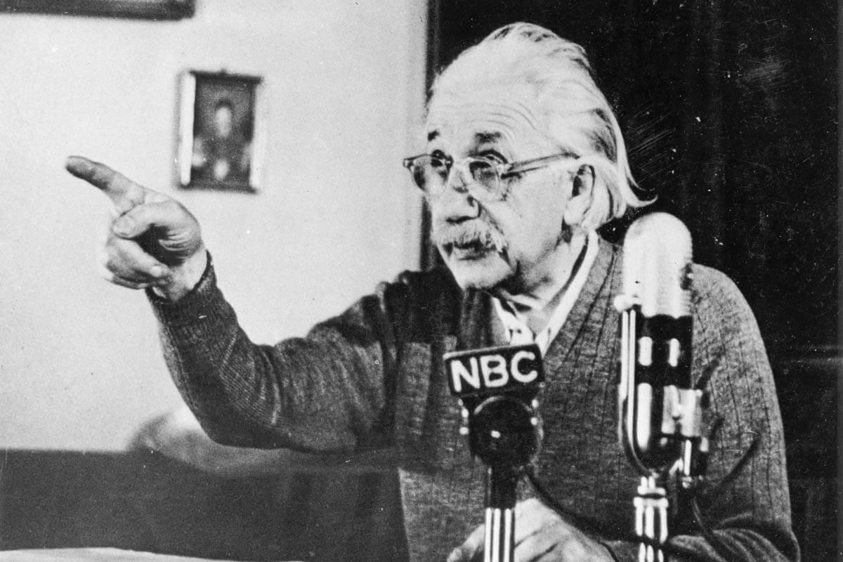 Albert Einstein giving a lecture in front of a microphone.