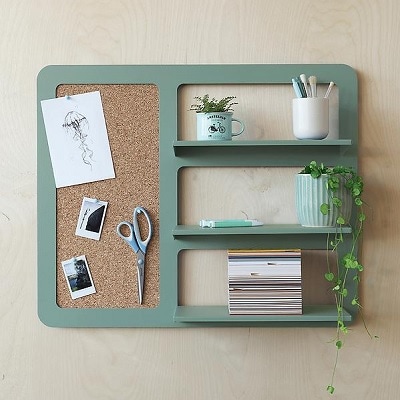 A green wall organizer with shelves and a bulletin board, holding plants and other items