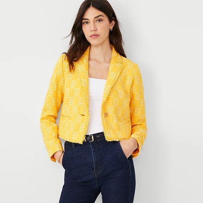 A woman wearing a yellow blazer, white top, and dark blue jeans